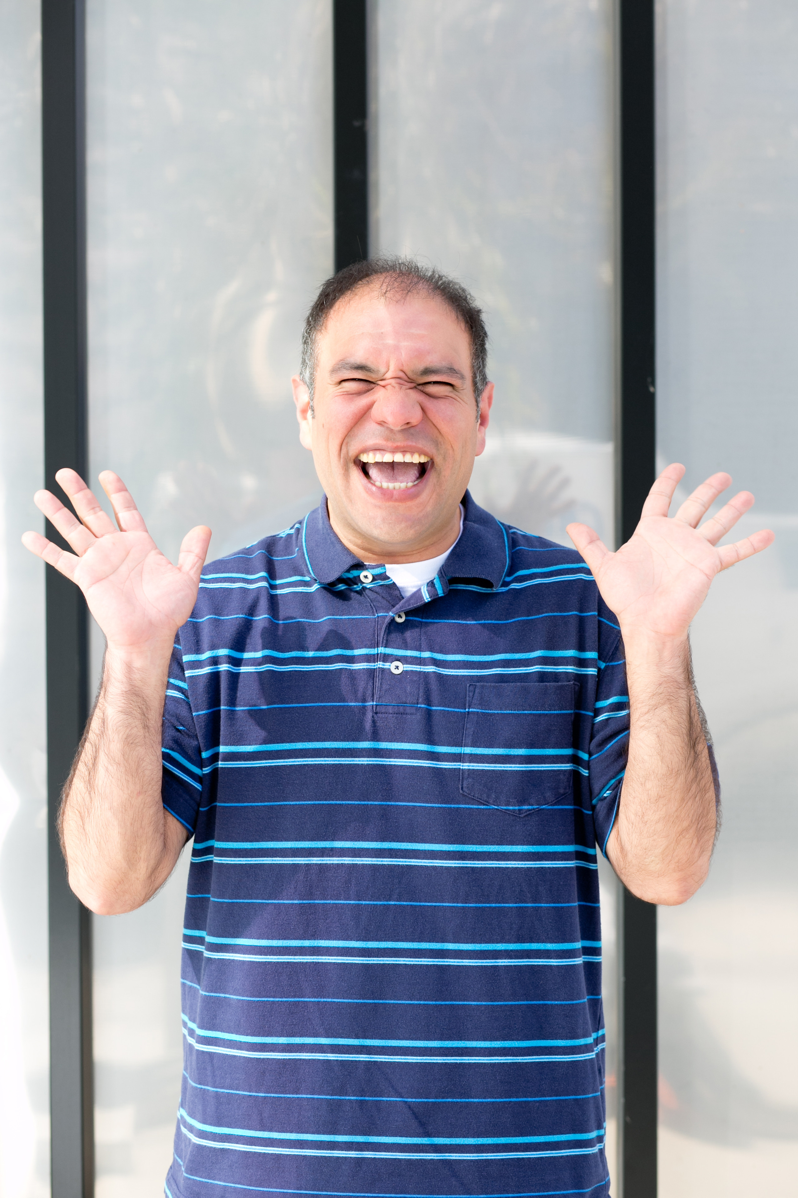 Melvin is standing in front of a window. He is doing jazz hands, and smiling enthusiastically.