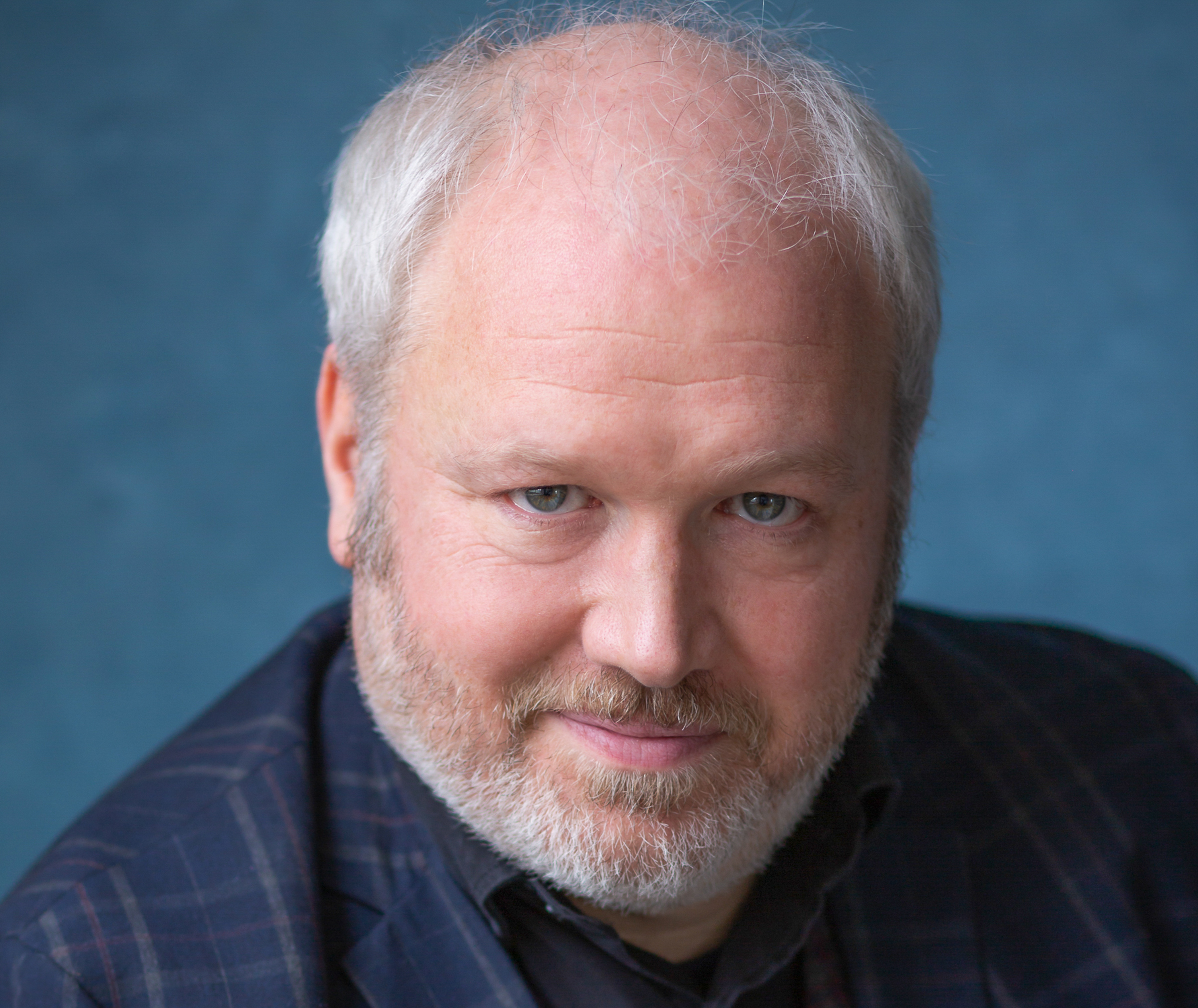 Handsome publicity shot of Toby, wearing a crooked smile and a very smart checked blue jacket.