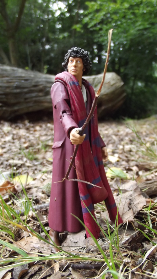 A Tom Baker action figure brandishing a twig, standing on the forest floor