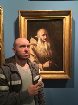 A young Brendan at an art gallery. He looks very serious. He is standing in front of a portrait of an eerily familiar-looking old man with a long grey beard who looks equally serious.
